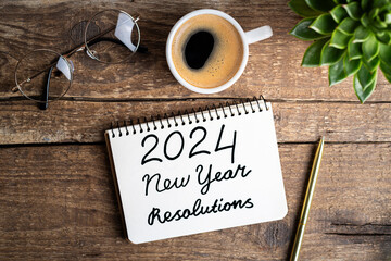 New year resolutions 2024 on desk. 2024 goals list with notebook, coffee cup, plant on wooden...