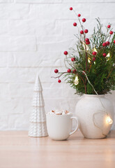 Christmas decoration - cup of cacao with marshmellows, christmas tree, branches fir in vase on coffee table on white bricks background.