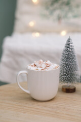 cup of cacao with marshmellows, christmas tree on coffee table on white pillow background.