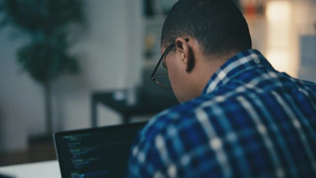 African American software tester checking code on laptop, working in office, IT
