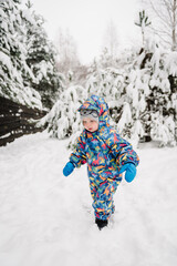 Fototapeta na wymiar Little child in blue winter clothes having fun. Kid wearing warm hat walking in winter park in holidays. Toddler in mountain country in snowy forest. Baby boy playing snow among snowdrifts closeup.