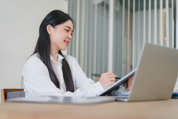 Successful Asian businesswoman looks confident and smiles while working with laptop in office.