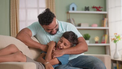 joyful Indian father cuddling his son on sofa at home - concept of Joyful Moment, Family Affection and Togetherness