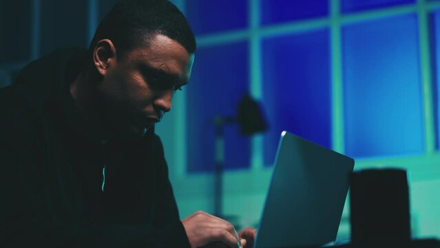 Serious African American man typing hacking code on laptop, breaching network