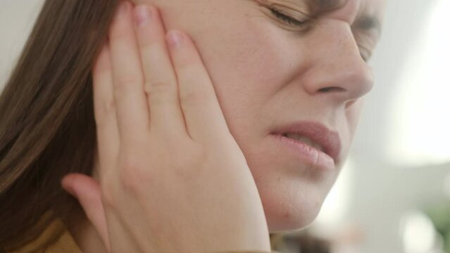 Closeup up side profile of sick sad young caucasian female having ear pain touching painful head sitting on sofa. Unhealthy tired woman suffering from painful otitis. Health care and tinnitus concept