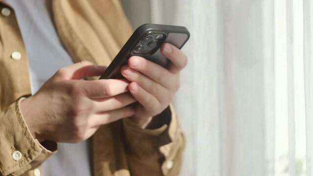 Close up of female hands use smartphone browse surf wireless internet on device standing near window at home. Push buttons, follow links. Morning Time phone using. Technology, communication concept