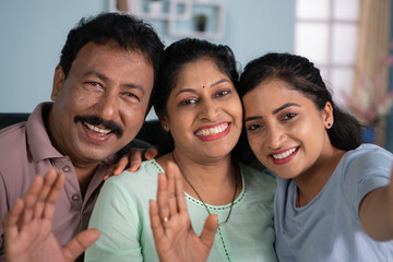Joyful Indian family or parents with daughter talking on video call at home - concept of Digital Communication, Family Bonding and distant relationship