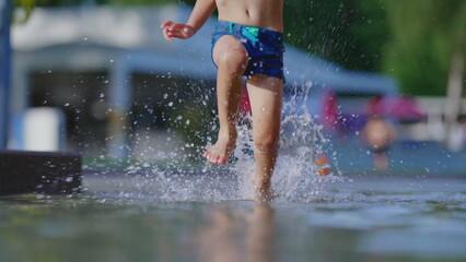 Active Little boy playfully Running in pool, causing water splashes at 120fps. Happy child sprinting during hot summer day