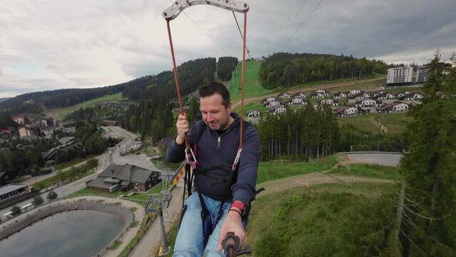 A man takes a selfie with a selfie stick while riding the zip line attraction.