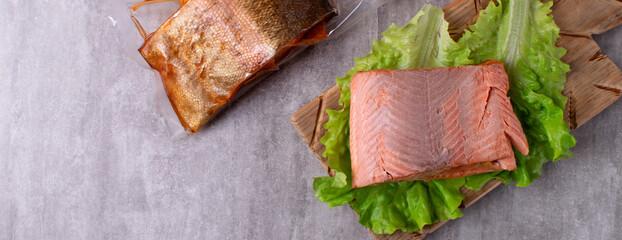 Hot smoked trout fillet piece on lettuce leaf on wooden board. Top view. Copy space