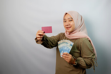 Happy beautiful Asian Muslim woman holding paper money and  showing credit card isolated on white background. ​