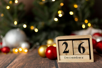Old vintage wooden calendar for the date of Christmas December 26 against the background of New Year's lights of garlands of bokeh light bulbs - obrazy, fototapety, plakaty
