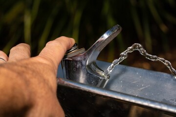 Closeup of a water drinking fountain with hand turning it on