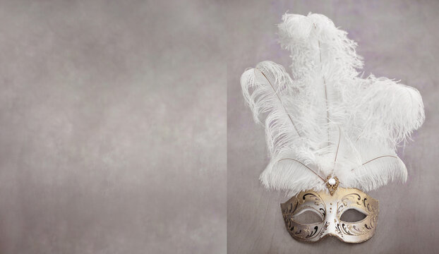 Gold tone Venetian carnival colombina mask with painted ornaments and huge white feathers. Minimal composition - a mask on a light colored pastel background