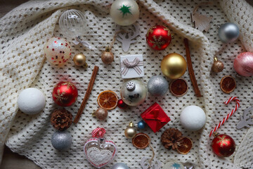 Various colorful Christmas ornaments, small presents and seasonal spices on white knitted blanket. Top view.