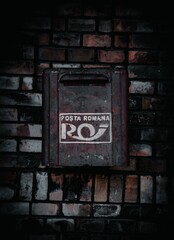 Old metal Romanian mailbox positioned on the side of a brick wall in an outdoor setting