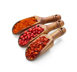 Crushed red pepper, paprika and peppercorn in wooden spoons isolated on white background