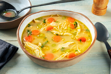 Chicken noodle soup with vegetables, a bowl of healthy broth with a ladle, on a rustic wooden...