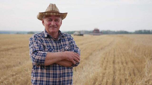 Happy adult farmer stands and smile at the camera against background of working tractor in field. Concept ecology, transport, outdoor nature, clean air, food. Natural production bio product.