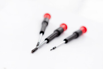 Close-up photoshoot of three red and black handled screwdrivers on a white background
