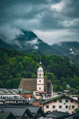 Fototapeta premium Vertical of a church tower in Berchtesgaden, Germany in green mountains on a cloudy day