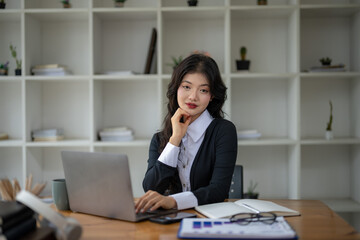 Freelance Asian woman sitting and working on laptop. Thinking, planning and focusing on the task.