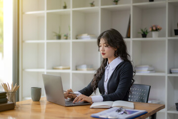 Freelance Asian woman sitting and working on laptop. Thinking, planning and focusing on the task.