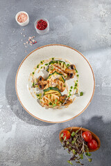 Close-up top view of a health-centric grilled turkey fillet steak with zucchini and mushrooms. The meal is set on a white ceramic plate and has a grey concrete background for a minimalist touch