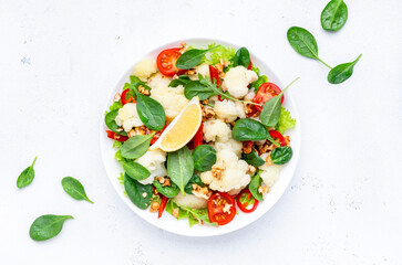 Useful vegan cauliflower salad with baked paprika, cherry tomatoes, spinach with walnuts, white table background, top view