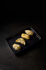 Vertical side view of traditional Uzbek manty presented on a black plate, beautifully contrasted against a black marble table