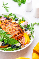 Tasty salad with peaches, grilled chicken breast, blueberries, red onion, feta cheese, basil and arugula, white table background, top view