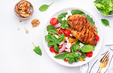 Healthy salad with grilled paprika and chicken, feta cheese, cherry tomatoes, walnut, red onion and lettuce, white table background, top view