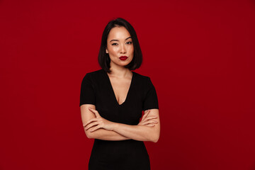 Pensive woman looking at camera while standing isolated over red wall