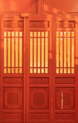 Obraz premium Yellow light passes through the red traditional Chinese wooden door with carved flowers.