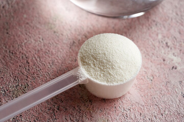 Collagen powder in a plastic measuring spoon on pink textured background