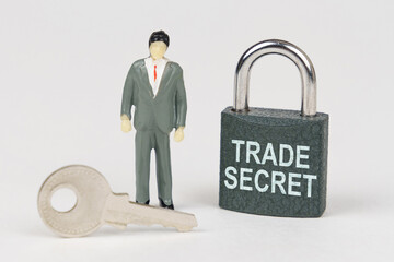 On a white surface there is a figurine of a businessman, a key and a lock with the inscription -...