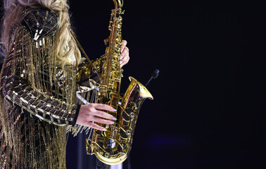 Woman playing on a golden saxophone against dark background. saxophone music.