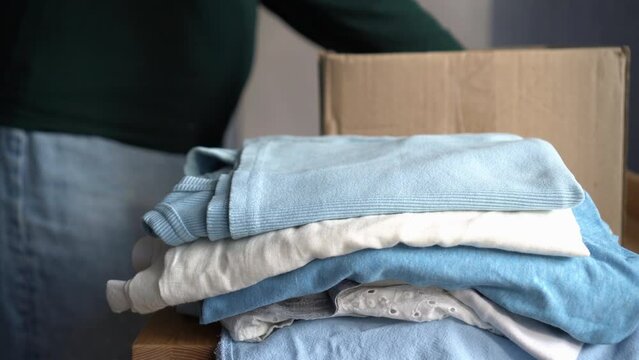 Concept of recycling clothes. Woman donates her clothes. Sale of used clothes. Moving to a new house, putting things in boxes