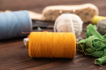 Sewing accessories: scissors, thread, thimbles, braid on brown wooden. Side view, selective focus