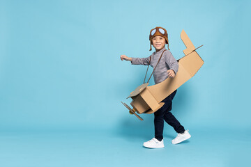 Asian little boy aviator playing with cardboard airplane isolated on blue sky background, Kid toy diy concept - obrazy, fototapety, plakaty