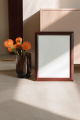 Empty vertical picture frame with shadows, flowers in vase on the floor in minimalist interior.