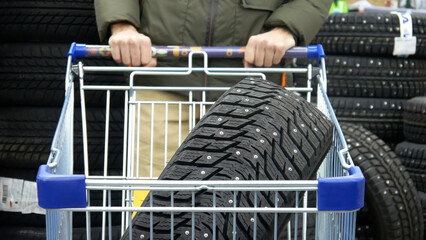 Close-up of a shopping trolley with winter tire and a male buyer rolls it