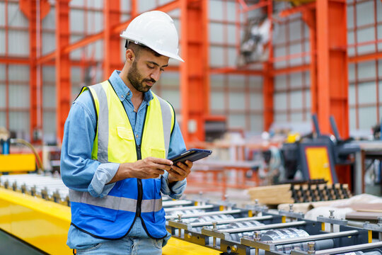 Professional Asian industrial engineer inspecting a heavy machine in metal sheet manufacturing factory.
