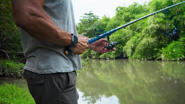 young guy with a fishing rod in his hands, twists a reel and fishes in a river in a rainforest.