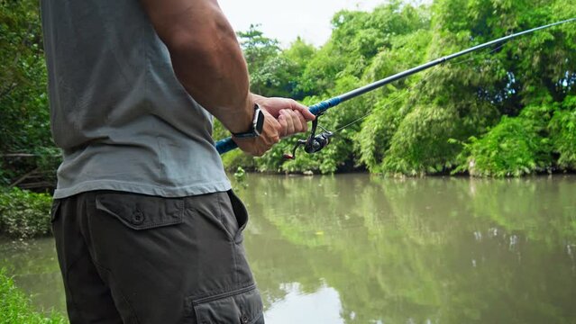 young guy with a fishing rod in his hands, twists a reel and fishes in a river in a rainforest.