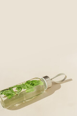 Glass bottle with green mint leaves water drink detox at sunlight on beige table background, copy space, sun glare. Natural Infused water Healthy drink. Aesthetic still life, refreshing drink