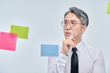 The businessman is standing on the glass wall of the office, looking at the paper attached,...