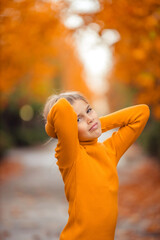 a teenage girl in a yellow sweater walks along a street outside the city against the backdrop of yellow trees. fun walk in autumn