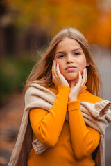 a teenage girl in a yellow sweater walks along a street outside the city against the backdrop of yellow trees. fun walk in autumn