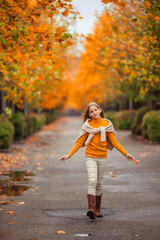 a teenage girl in a yellow sweater walks along a street outside the city against the backdrop of yellow trees. fun walk in autumn